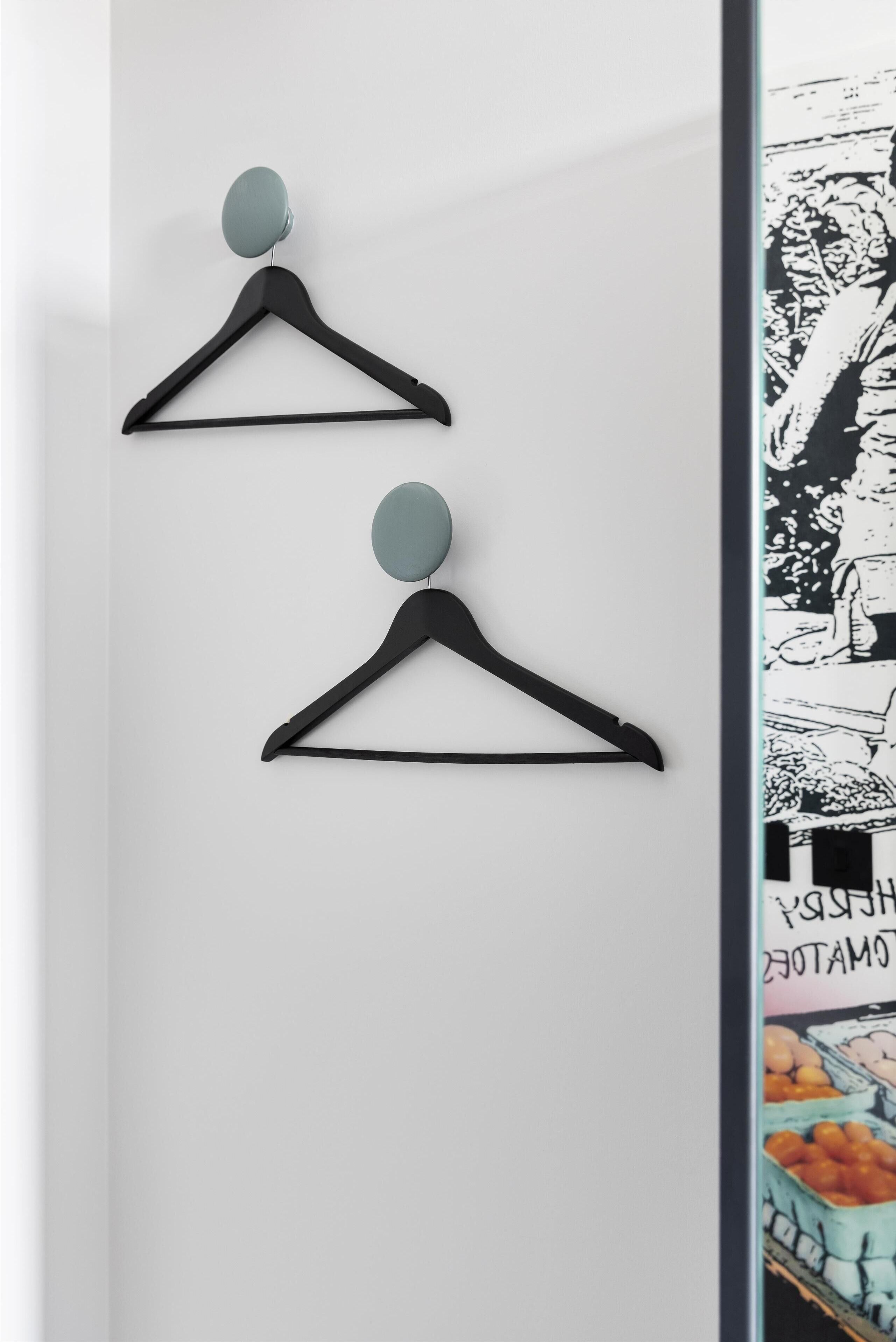 Two black wall-mounted hangers with light blue knobs on a white wall.