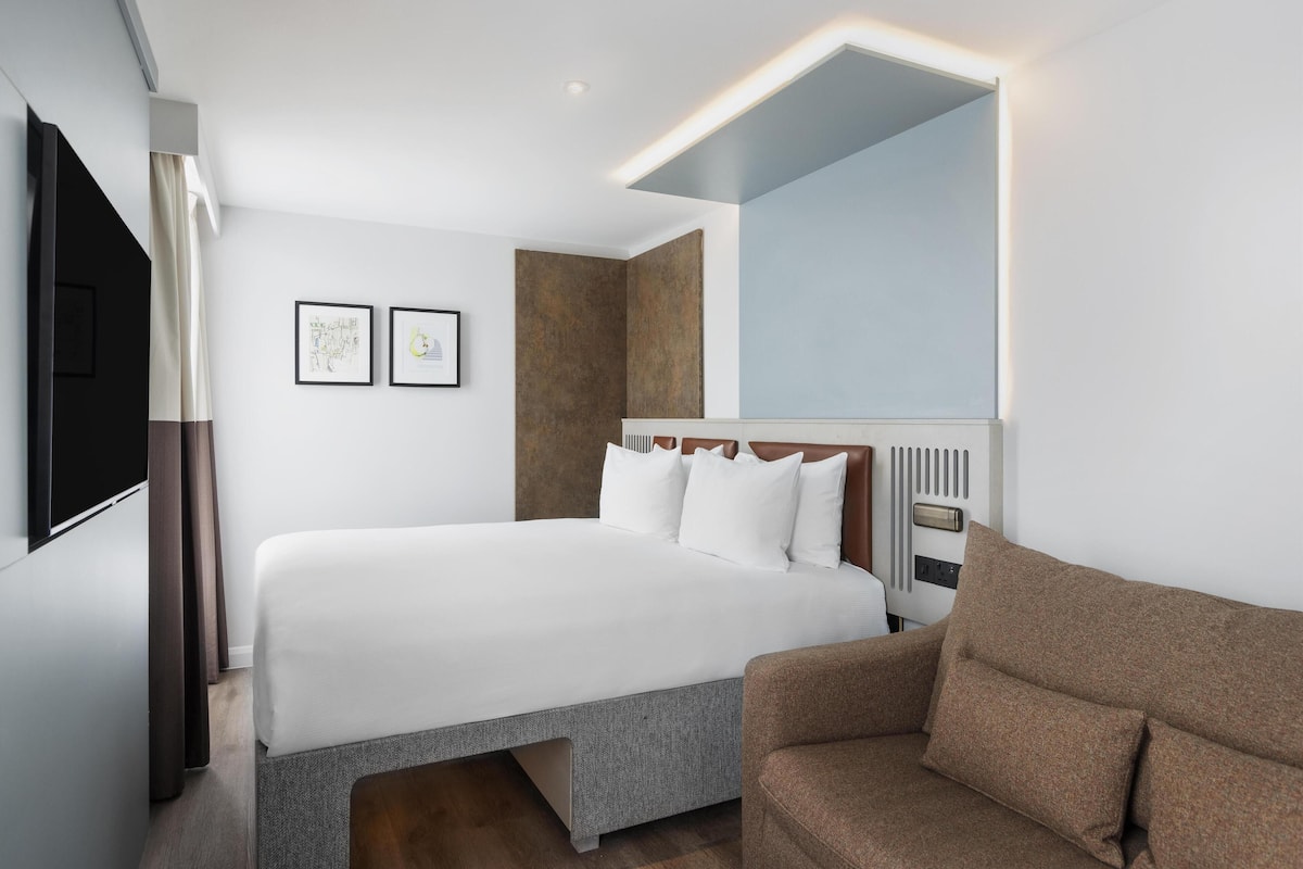 A modern hotel room with a large bed, a brown sofa, and a flat-screen TV.