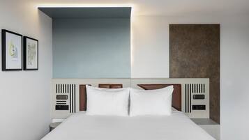 A modern hotel room with a large bed, a headboard with built-in controls, and framed artwork on the wall.