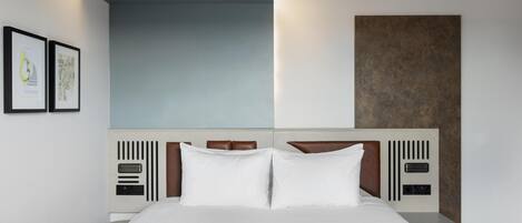 A modern hotel room with a large bed, a headboard with built-in controls, and framed artwork on the wall.