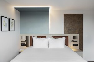 Una habitación de hotel moderna con una cama grande, un cabecero con controles integrados y cuadros en la pared.