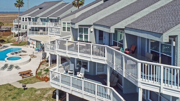 A multi-story residential building with balconies, a swimming pool, and outdoor seating areas. - Pool w/ Spa! Beachfront Condo in Port Aransas (Port Aransas)