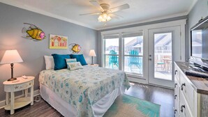 A bedroom with a bed, two bedside tables, a ceiling fan, and a view of the outside balcony. - Pool w/ Spa! Beachfront Condo in Port Aransas (Port Aransas)