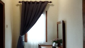 A narrow hallway with a wooden ceiling, a radiator, a window with dark curtains, a wooden desk with a mirror, and a small rug on the floor. - Balkondes Borobudur Duta Menoreh (Magelang)