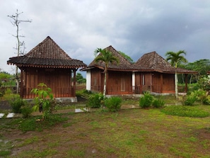 Deux maisons en bois aux toits de tuiles, entourées de verdure et surplombées par un ciel nuageux.
