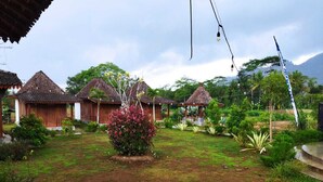 A traditional wooden house with a thatched roof, surrounded by lush greenery and a well-maintained garden. - Balkondes Borobudur Duta Menoreh (Magelang)