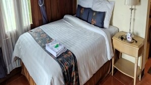 A neatly made bed with a floral bedspread, a bedside lamp, and a small table with a lamp. - Balkondes Borobudur Duta Menoreh (Magelang)
