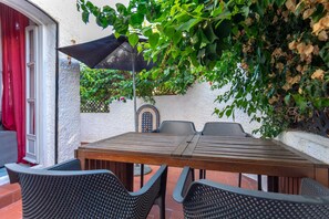 Eine Außenpatio mit einem Holztisch und vier Stühlen, einem schwarzen Sonnenschirm und einer mit Kletterpflanzen bewachsenen Mauer.