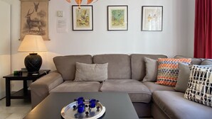 Ett modernt vardagsrum med en grå soffa, ett soffbord med ett bricka fullt av blå koppar, en lampa och tre inramade konstverk på väggen.