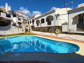 Piscina com arco de pedra, edifícios brancos com janelas em arco e um círculo de boia na borda.