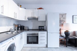 Eine kleine Küche mit weißen Schränken, einem eingebauten Backofen, einer Mikrowelle und einem Kühlschrank.