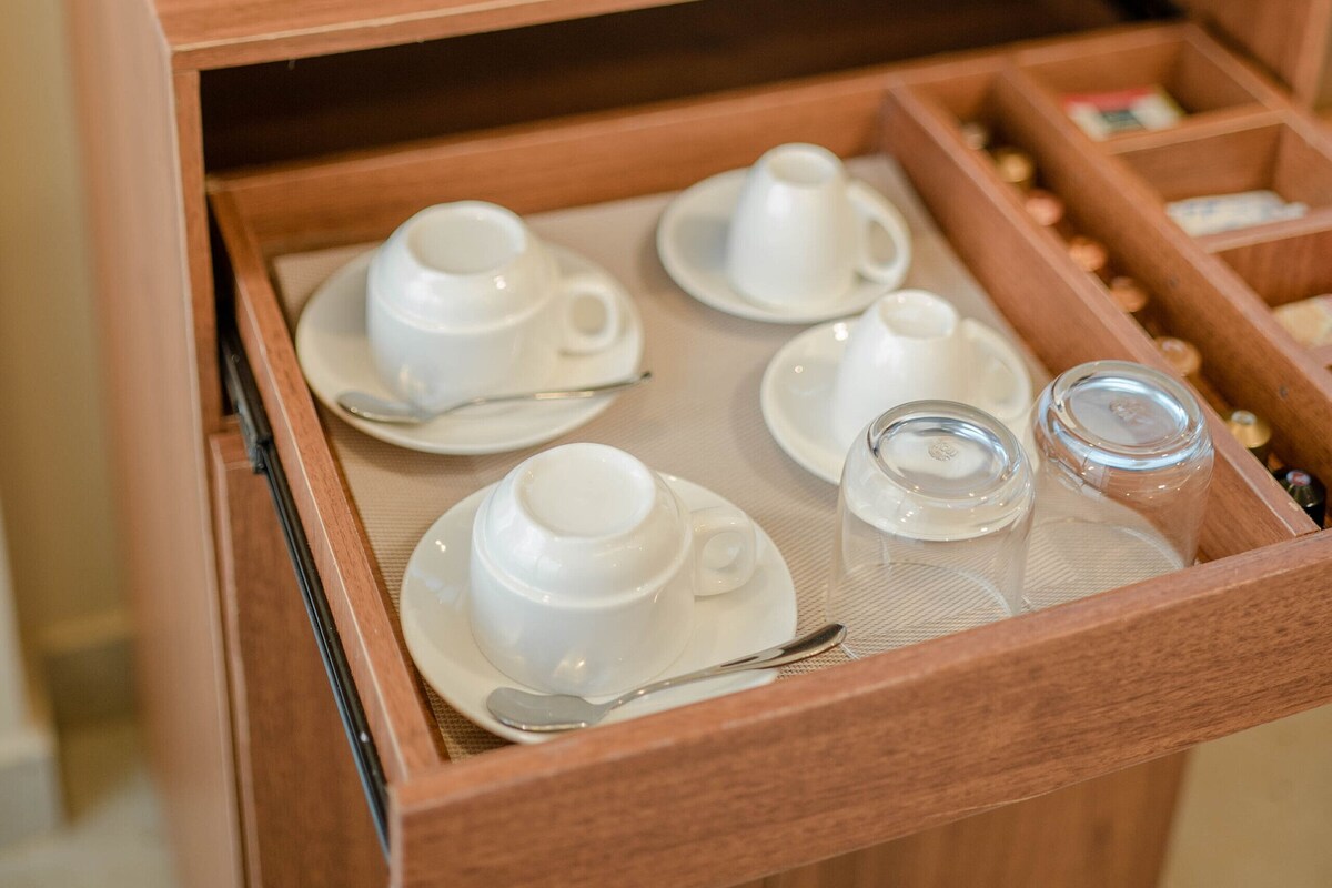 A wooden tray with cups, a coffee maker, and bottled water.