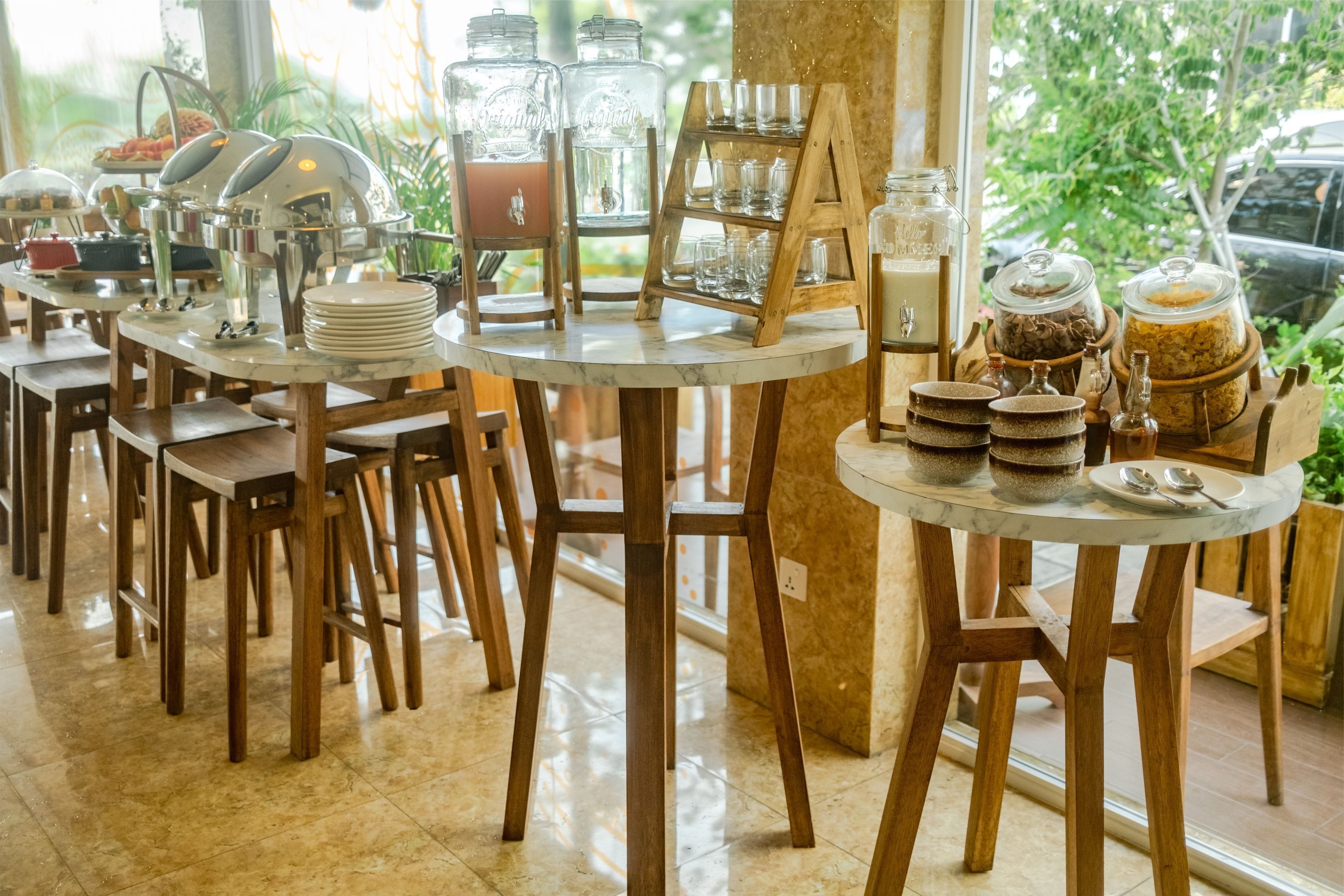 Un comedor con mesas redondas, sillas de madera y varios dispensadores de comida y bebida.