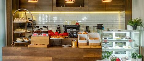 A modern kitchen with wooden cabinets, a coffee machine, and a display case with pastries.