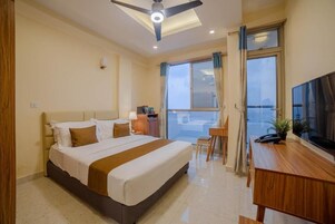 Habitación de hotel con cama, escritorio, silla, televisor y balcón con vistas.