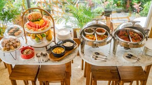 A buffet table with various dishes and utensils, surrounded by wooden chairs and potted plants. - Amber Beach (Hulhumalé)