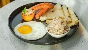 A plate with a fried egg, grilled sausage, flatbread, and a small bowl of a white spread. - Amber Beach (Hulhumalé)