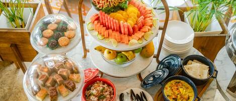 Une table de buffet proposant divers plats, dont un centre de table composé de fruits et de légumes, un saladier de biscuits et plusieurs plats servis dans des récipients.