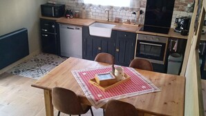 A compact kitchen with a brick wall, a sink, a stove, and a dining area with a table and chairs. - Comfortable cottage "Les Délices" (Guewenheim)