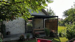 A stone building with a wooden deck, a red chair, and a slide. - Comfortable cottage "Les Délices" (Guewenheim)