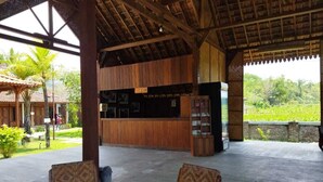 A covered outdoor area with a reception desk, wicker chairs, and a view of a lush landscape. - Balkondes Borobudur Karanganyar (Magelang)