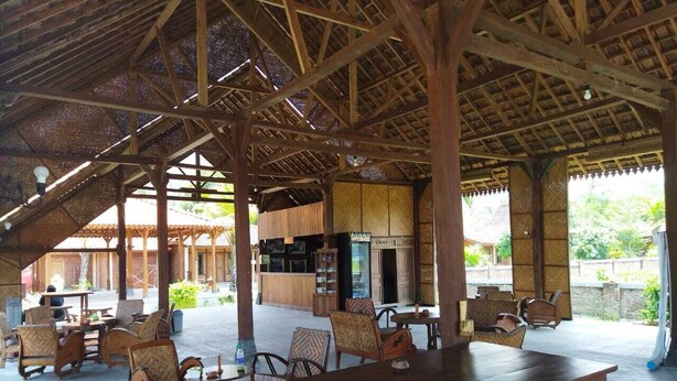 An outdoor covered seating area with wooden tables and chairs, a bar area, and a view of a tropical landscape. - Balkondes Borobudur Karanganyar (Magelang)