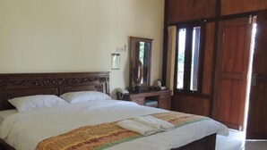 A large bed with a wooden headboard, a bedside table with a mirror, and a window with curtains. - Balkondes Borobudur Karanganyar (Magelang)