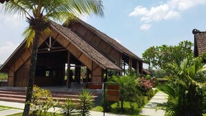 A traditional wooden building with a tiled roof, surrounded by a well-maintained garden with palm trees and a clear pathway leading to the entrance. - Balkondes Borobudur Karanganyar (Magelang)
