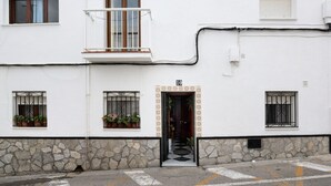 A building with a stone base, a balcony, a door with a number, and potted plants.