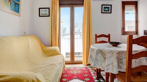 A room with a bed, a dining table with chairs, a balcony with curtains, and a painting on the wall.