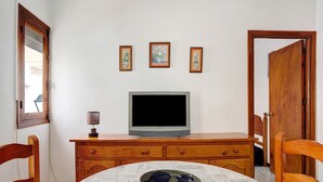 A room with a television on a wooden cabinet, a dining table with a decorative plate, and three framed pictures on the wall.