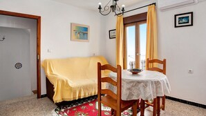 A room with a bed, a dining table with chairs, a chandelier, and a window with curtains.