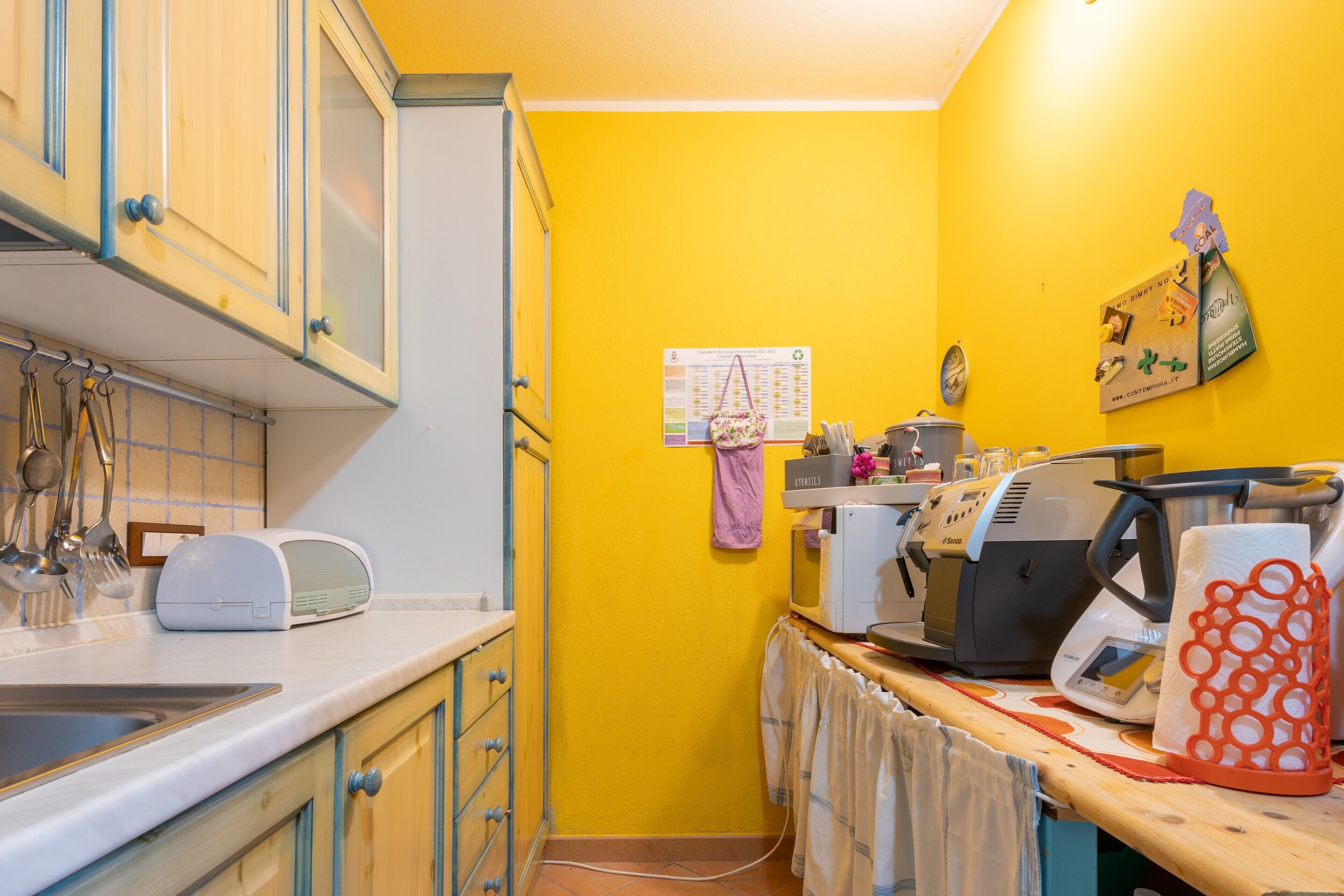 A kitchen with yellow walls, a sink, cabinets, a toaster, a kettle, and a coffee maker.