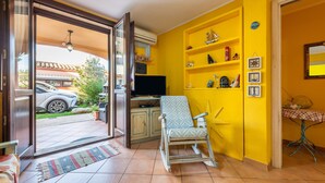 Ein Wohnzimmer mit Fernseher, Schaukelstuhl, gelber Wand und einer zur Außenseite führenden Tür.