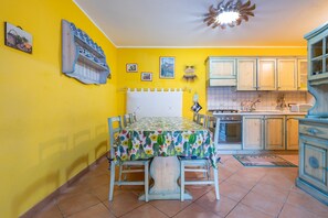 A room with a dining table, chairs, a bed, a kitchen area, and a ceiling fan. - Villa Gialla Castiadas with Mountain View, Terrace & A/C (Castiadas)