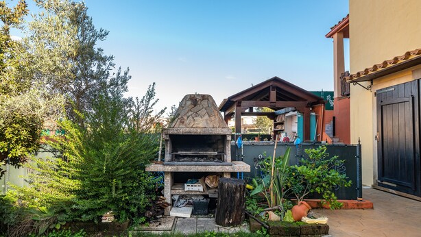 Un four extérieur en pierre, une pergola en bois et une maison avec une porte sombre.
