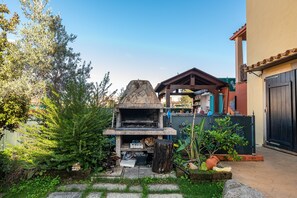 Ein Steinofen im Freien, eine Holzpergola und ein Haus mit einer dunklen Tür.