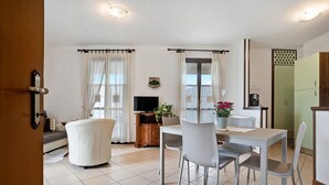 Un área de comedor con una mesa y sillas, un sofá, un televisor y un armario.