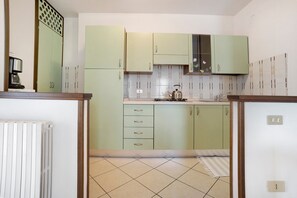 Una cucina con mobili verdi, zoccolo in piastrelle e bollitore sul piano di lavoro.