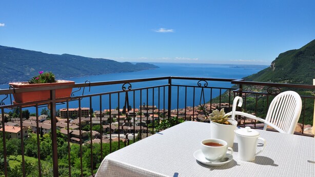 Un balcón con una mesa preparada para dos personas, con vistas a un pueblo costero y al mar.