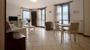 Un salon comprenant un canapé, un téléviseur, une table à manger, des chaises et une plante en pot.