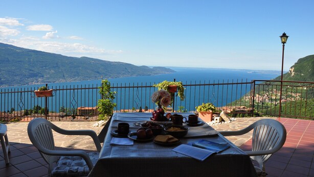 Une terrasse avec une table dressée pour le petit-déjeuner, offrant une vue imprenable sur un lac pittoresque et les montagnes.