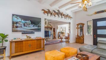 A spacious living room with a large TV, wooden furniture, a stone fireplace, and a chandelier.