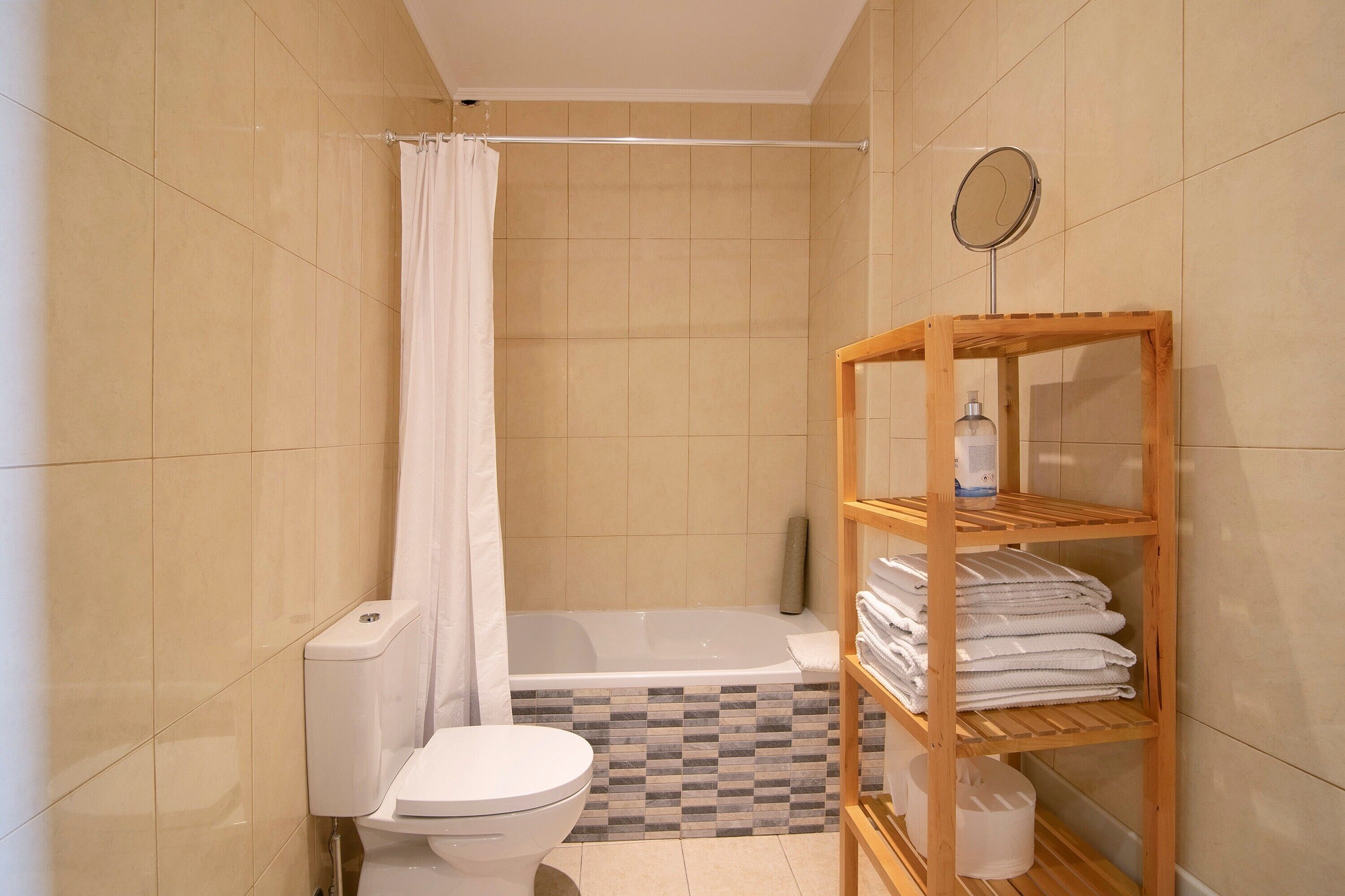 A bathroom with a toilet, a shower with a curtain, a bathtub, and a wooden shelf with towels.