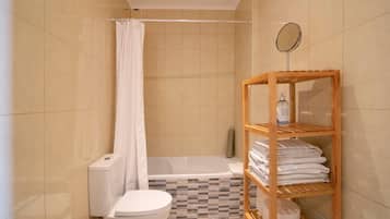 A bathroom with a toilet, a shower with a curtain, a bathtub, and a wooden shelf with towels.