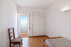 Quarto com cadeira de madeira, cama, guarda-roupa e porta que dá para o exterior.