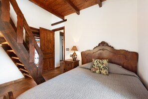 Une chambre à coucher avec une tête de lit en bois, un lit agrémenté d’un coussin à motifs floraux, une table de chevet avec une lampe et un escalier en bois.