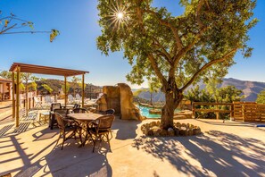 Un espace patio aménagé avec du mobilier d’extérieur, une pergola, un arbre et une vue sur un paysage montagneux.