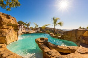 A natural pool surrounded by rock formations, with a clear view of the landscape and a sunlit sky.