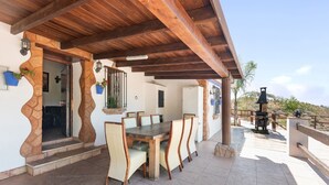 A covered patio with a wooden table and chairs, stone walls, and a view of the surrounding landscape. - Pet-Friendly Vacation Home 'Miramar' with Garden, Private Pool, Terrace & Wi-Fi (Almogia)